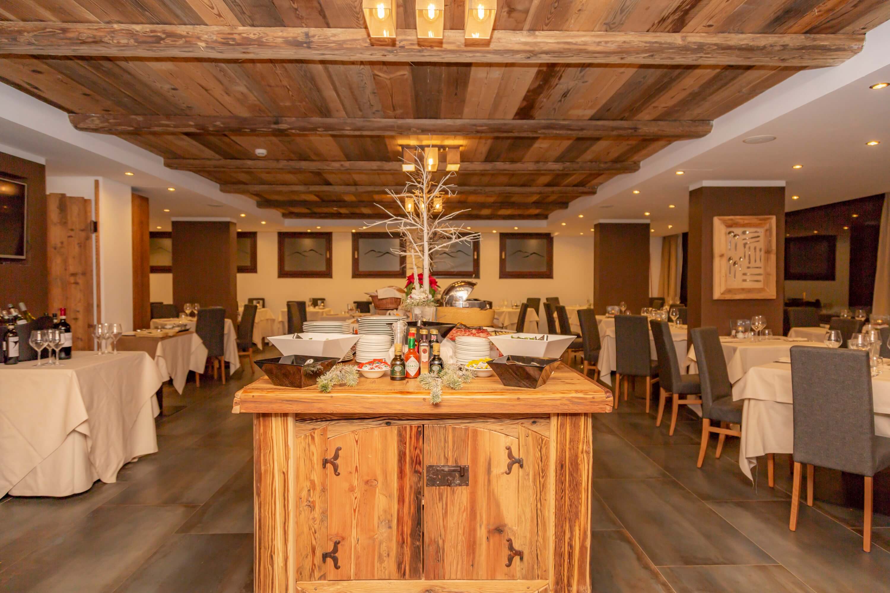 Rustic dining room with a wooden table, warm lighting, exposed beams, and artwork, creating a cozy, inviting atmosphere.